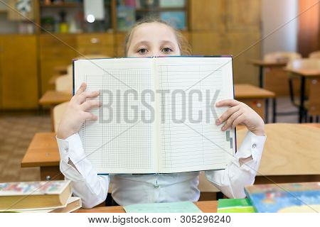 The Schoolgirl Covered Her Face With A School Gradebook. A Teenager Girl Hides Her Face Behind An Op