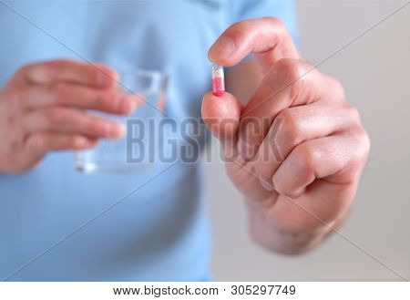 A Man With A Glass Of Water In His Hand. Elevated Body Temperature. Cold And Flu Pills. Prevention A