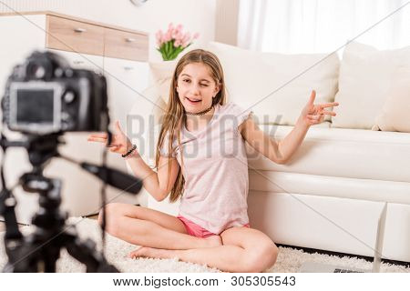 Young smiling videobloger teen girl is pointing at camera in living room