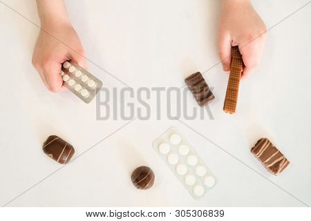 Child Holds In One Hand A Package Of Pills And Sweet Iris In The Second Hand. Concept Of Dangerous D