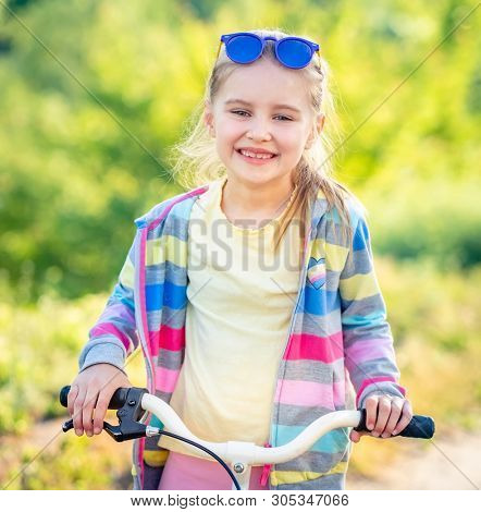 Adorable smiling girl riding small modern bike with colorful jacket outdoors