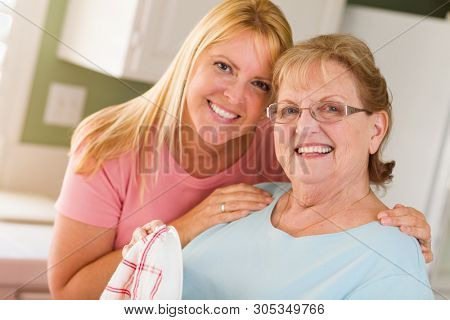 Portrait of Smiling Senior Adult Woman and Young Daughter At Sink in Kitchen.