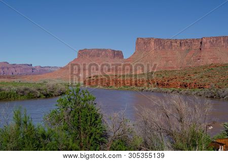 Red Rock Mountains Overlooking A River With Trees In The Foreground.  Near Arches National Park, Uta