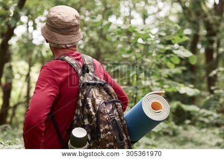 Senior Backpackers Walking Along Road In Forest, Eldery Traveller Wears Red Casual Sweater, Cap, Ruc