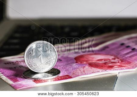 Close Up View Of One Rupee Coin Over Brand New Indian 2000 Rupees Banknotes And  Laptop.