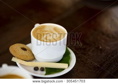 A Cup Of Hot Coffee On White Plate With Cake, Peace Of Cane And Leaves. Placed On Old Bar Counter. C