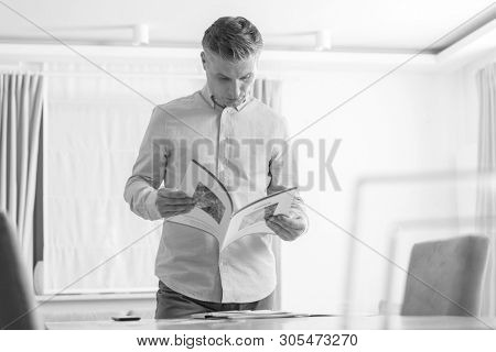 Black and White photo of Mature man reading brochure while standing at table in apartment