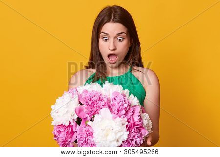 Portrait Of Impressed Worried Cute Young Lady Looking At Bouquet Of Flowers With Shock, Opening Mout
