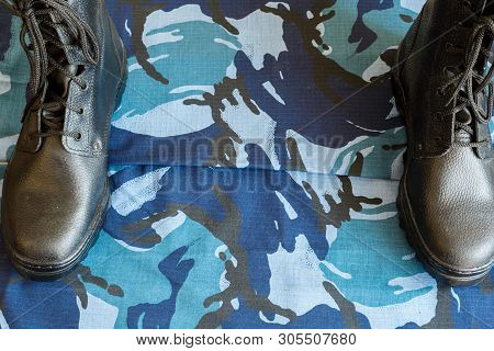 A Pair Of Black Army Boots On Fabric With Blue Camouflage With Copispace For Text.