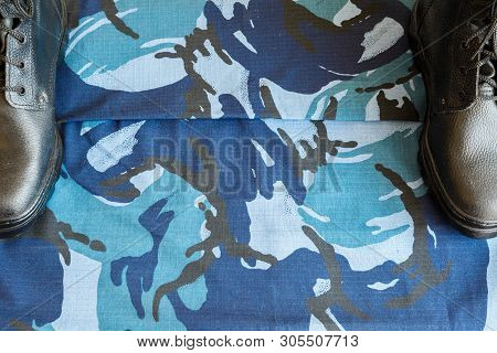 A Pair Of Black Army Boots On Fabric With Blue Camouflage With Copispace For Text.