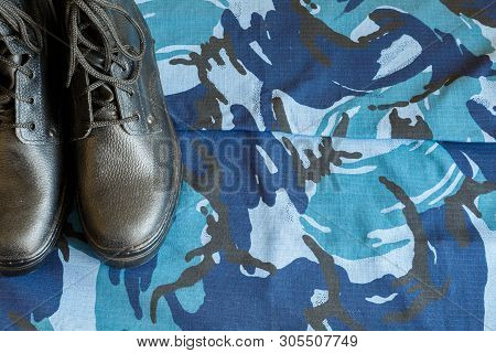 A Pair Of Black Army Boots On Fabric With Blue Camouflage With Copispace For Text.
