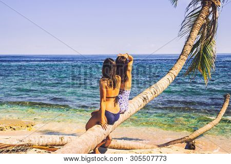 Two Girls Sitting On Palm Tree On The Beach. Healthy People Lifestyle. Girls Relaxing On The Beach. 