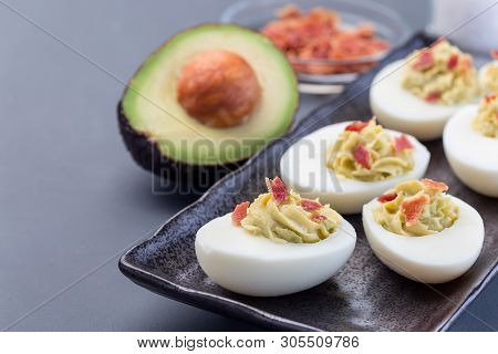 Deviled Eggs Stuffed With Avocado, Egg Yolk And Mayonnaise Filling, Garnished With Bacon, Horizontal