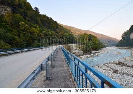 Panorama Mountain Road Across The River, With A Bridge With Blue Railings In The Cherek Gorge In The