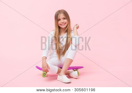 Enjoying Vibes On Penny Board. Cute Little Child Sitting On Penny Board Deck On Pink Background. Ado