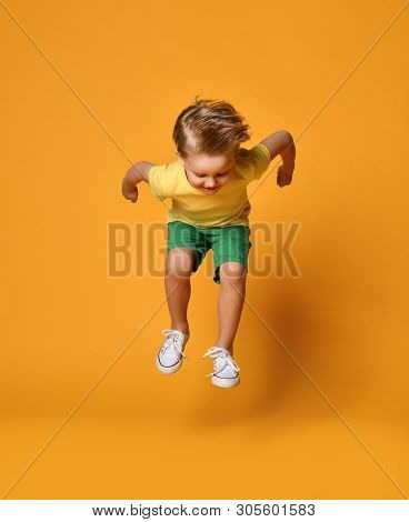 Full Length Portrait Of An Excited Young Boy Jumping Leaping In Green Shorts Over Yellow Background