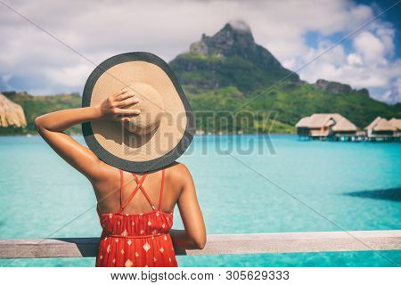 Beach vacation travel getaway summer holiday woman looking at view of Mt Otemanu on Bora Bora luxury hotel on romantic honeymoon. Tourist holding hat from behind enjoying Tahiti, French Polynesia.