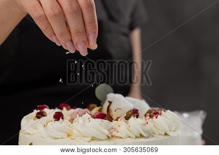 The Condater Sprinkles The Cake With Grated Almonds And Coconut. Close-up Of A Hand And Pouring Crum