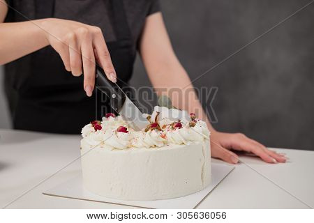 A Condater Cuts A Beautiful Fresh Decorated White Cake With A Large Knife.