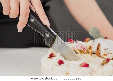 A Condater Cuts A Beautiful Fresh Decorated White Cake With A Large Knife.
