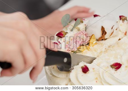A Condater Cuts A Beautiful Fresh Decorated White Cake With A Large Knife.