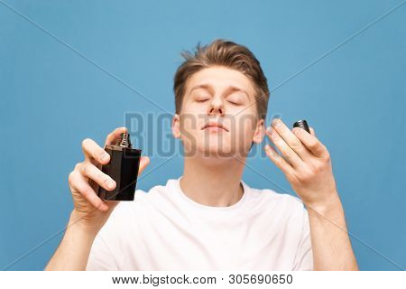 Close Up Portrait Of A Boy In A White T-shirt Stands On A Blue Background, Spray Perfume And Smells 