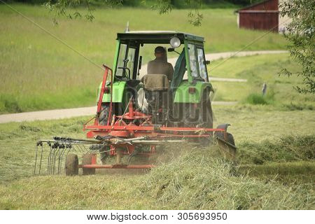 Farmer With Tractor And Hay Tedder At The Hay Harvest