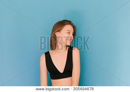 Portrait Of A Happy Girl Of Model Appearance On A Blue Background, Wearing A Bra, Looking Away And S
