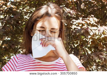 Young Girl With Allergy In Autumn Park. Sneezing Girl Blows Her Nose In A Napkin