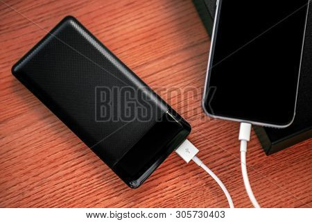 powerbank charges smartphone isolated on wood background