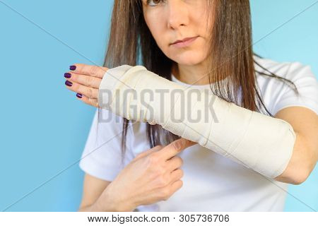 Middle Aged Woman With Broken Arm Bone In Cast, Plastered Hand On Blue Background. Selective Focus O