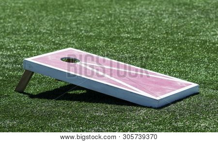 A Red And White Homemade Wooden Cornhole Board Is On A Green Turf Field.