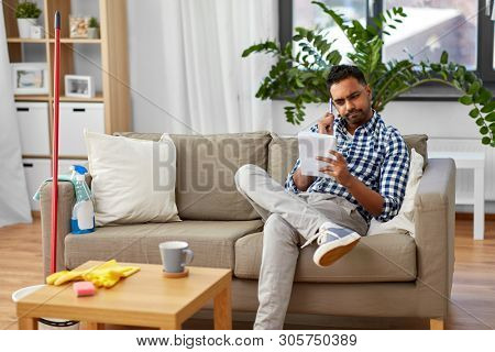household and time management concept - indian man making to do list in notebook after home cleaning
