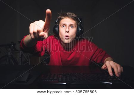 Amazed Young Man Sitting At The Table At The Computer At Home, With Astonished Face Looking At The S
