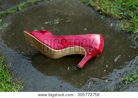 Red Highheel Abandoned On The Asphalt, Wet After Rain, Outdoor Close-up