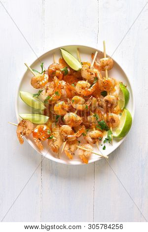Tasty Prawns Skewers With Greens, Spices, Lime And Sauce On White Plate Over Wooden Table. Grilled S