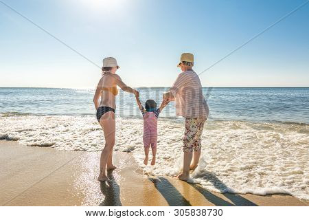 Mother, Daughter And Grandmother Playing In The Waves At The Beach