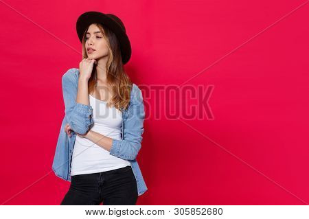 Fashionable Girl In Casual Clothes And Brown Hat, Posing With Attitudine In Studio Over Light Red Ba
