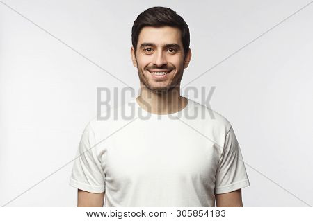 Portrait Of Smiling Young Man In White T-shirt Looking At Camera, Isolated On Gray Background