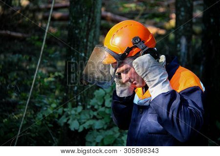 Lumberjack With Headphones In The Forest.lumberjack In Protective Safety Work Wear With Chainsaw At 