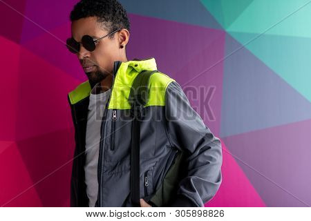 Serious Black Male In Stylish Shades And Jacket Standing Near Colorful Geometric Graffiti Wall