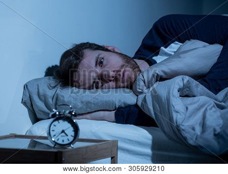 Young Man In Bed Staring At Alarm Clock Trying To Sleep Feeling Stressed And Sleepless