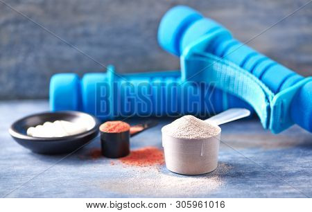 Scoop Of Whey Protein, Creatine Powder, Taurine Capsules And Blue Dumbbells In Background. Sport Nut