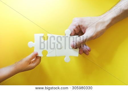 Child And Father Hands Taking Pieces Of Puzzle. Happy And Friendly Family Concept. Bright Yellow Bac