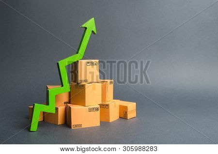 A Pile Of Cardboard Boxes And A Green Up Arrow. The Growth Rate Of Production Of Goods And Products,
