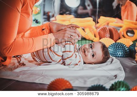 Happy Smiling Cute Toddler Is Lying On The Special Table Surrounded By Ortopedic Toys While Expirien