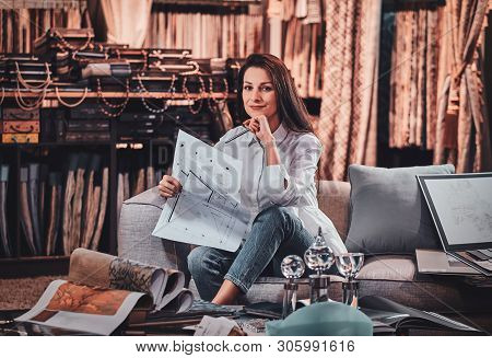 Attractive Pensive Woman Is Sitting On The Sofa At Her Curtians Atelier While Handing Drawings About