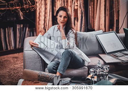Attractive Pensive Woman Is Sitting On The Sofa At Her Curtians Atelier While Handing Drawings About