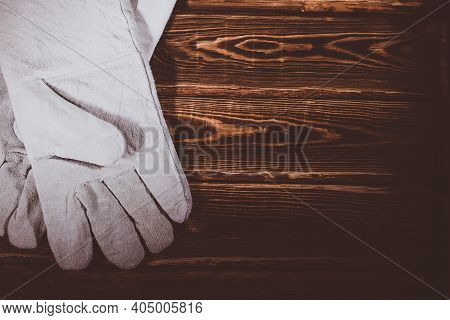 White Leather Welder Gloves On A Wooden Background. A Studio Photo With Hard Lighting.