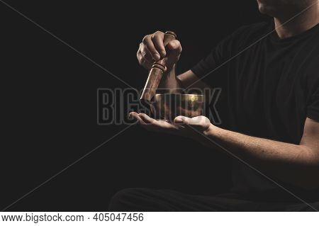 Detail Of Man Sitting Playing The Tibetan Singing Bowll In Black Clothes On Black Background.
